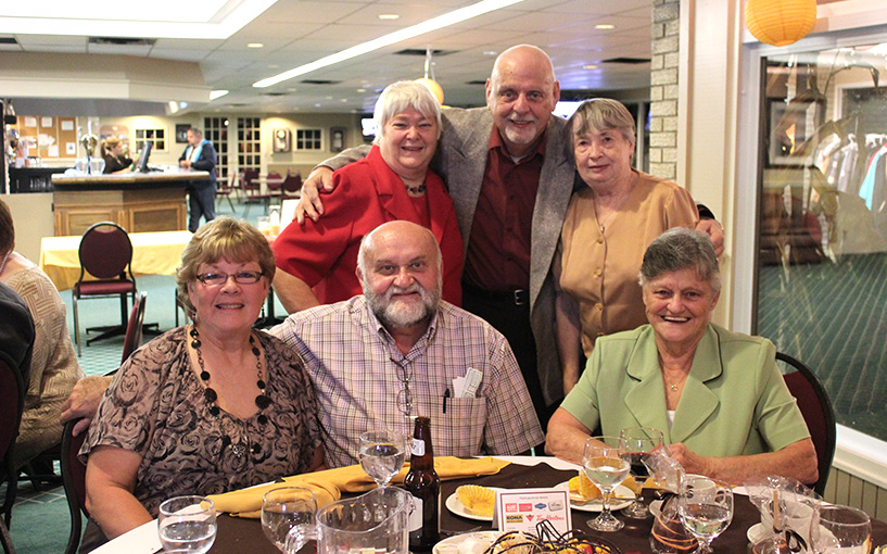 group of older people sitting posing for photo and looking at camera around a table